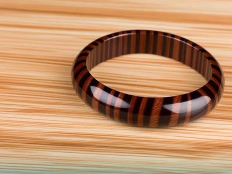 Chiếc vòng tay gỗ mun sọc sang trọng nằm trên nền gỗ tự nhiên.